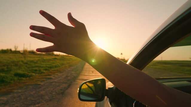 Young woman driver drives car, catches wind with her hand from car window. Free girl in front seat of car, sticking her hand out window, catching wind, glare of sun. Family, child traveling by car