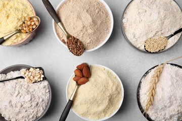Bowls with different types of flour and ingredients on light grey table, flat lay