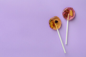 Sweet colorful lollipops with berries on lilac background, flat lay. Space for text