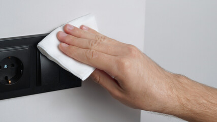 Man cleaning light switch with wet wipe indoors, closeup. Protective measures
