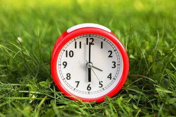 Red alarm clock on green grass outdoors