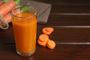 Glass of tasty carrot juice on wooden table, closeup. Space for text