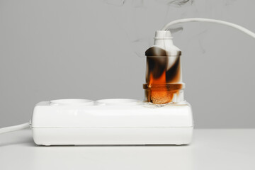 Inflamed plug in power strip on white table against grey wall. Electrical short circuit