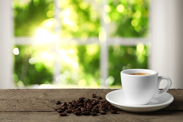 Cup of aromatic coffee and beans on wooden table indoors, space for text