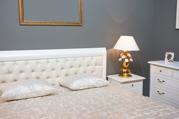 Luxury and expensive bedroom interior with white bad, golden lamp, ivory commode and golden frames