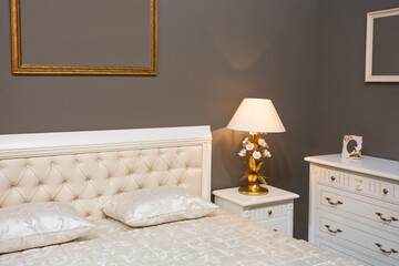Luxury and expensive bedroom interior with white bad, golden lamp, ivory commode and golden frames