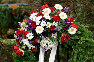 Fototapeta na wymiar funeral wreath in a cemetery with colorful flowers and bow on a metal stand