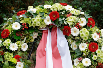 funeral wreath in a cemetery with colorful flowers and red and white bow on a metal frame