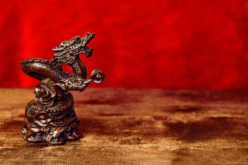 Carved wooden Asian Tibetan dragon statue against red background on wooden table for Chinese lunar new year left side