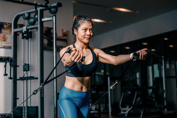 Fototapeta na wymiar Asian woman doing exercises with crossover cable machine exercises in the gym. Fitness, healthy style concept.