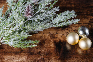 Winter evergreen tree branch with pinecones and frost and silver and gold Christmas ornaments on wood table closeup