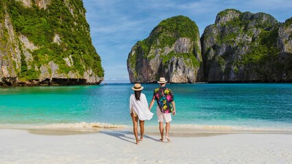 The backside of Thai women and caucasian men with a hat walk on the beach of Maya Bay, beach Koh...