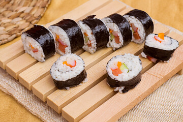 Close up a set of fresh and cheap japanese sushi rolls with crabstick, cucumber, carrot and sausage served on a wooden board