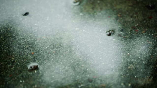 梅雨、砂利の地面の水たまりに雨の水滴が落ちて波紋を残すスローモーション