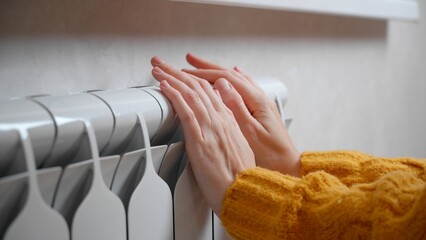 Women's hands are trying to keep warm on an aluminum radiator. A woman warms herself by a radiator...