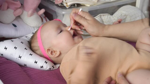 Young mother cleaning baby nose with cotton swab on changing table. Hygiene and healthcare of infant concept