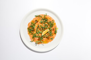 Salmon carpaccio with arugula on white background in summer day. Fish appetizer - salmon carpaccio in fine dining with shadows. Elegant carpaccio of raw salmon and sauce. Italian food. Aesthetic menu.