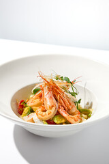 Elegant food - salad with shrimp and avocado on white table with harsh shadow. Flashy food concept. Seafood salad with shrimp, tomatoes and avocado on white plate with sunlight.