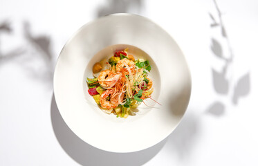 Elegant food - salad with shrimp and avocado on white table with harsh shadow. Flashy food concept. Seafood salad with shrimp, tomatoes and avocado on white plate with sunlight.
