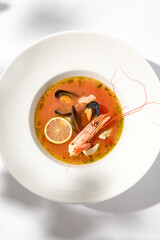 Traditional italian fish soup with shrimp, mussels and salmon. Seafood soup on white background. Tom yam kung with seafood. Spicy fish soup with prawns and lime on light background. Trendy food.