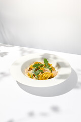 Italian ravioli with meat and mushroom sauce on white plate. Meat tortellini with creamy sauce in summer menu with shadows of tree leaves Ravioli stuffed beef in elegant style