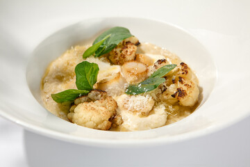 Seafood risotto with scallops and cauliflowers on white plate. Creamy risotto with sea scallops and cauliflowers. Italian risotto with sea scallops on light background with shadows of leaves