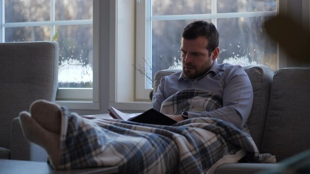 Person sits in couch researching genealogy, reads book about family history