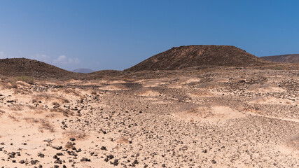 Wide light dry desert landscape with black volcanic rocks and elevations in distance