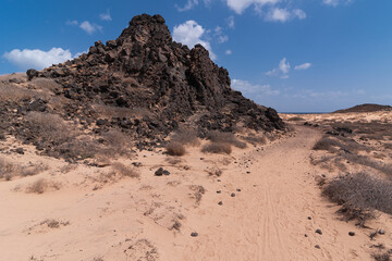Dark volcanic hill next to desert road leading to lighthouse, Lobos Island, Spain
