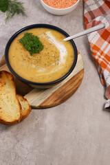 red lentils soup puree in dark bowl with bread on grey marble table