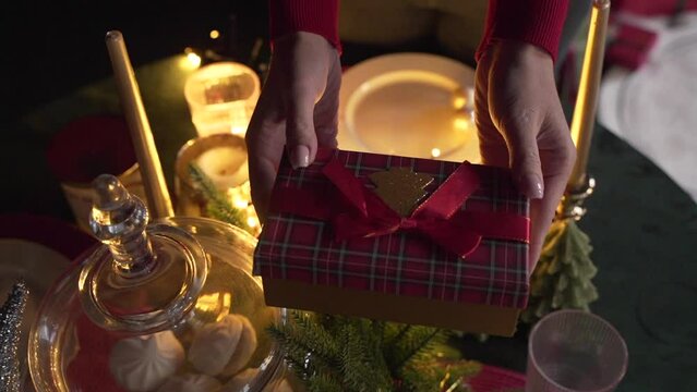 Close up of woman's hands give a gift near the Christmas tree 