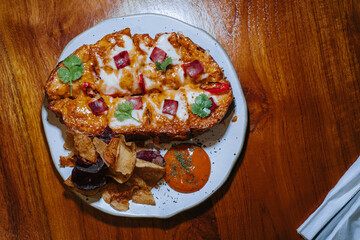 Flat lay or top view of a plate of Open Face Sourdough Beef Sandwich that contains sourdough, cheese sauce, mozzarella cheese sauce, creamy oriental sauce sauce and smoked beef in the wooden table