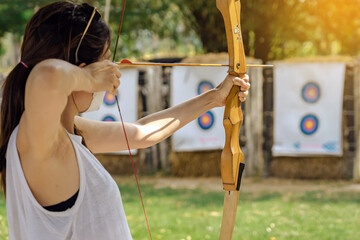 Hands of woman aims archery bow and arrow to colorful target in shooting range during training....