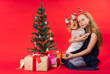 Girls, children with gifts and christmas trees. Christmas. Studio. Red background