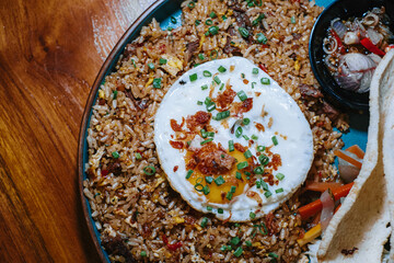 Flat lay or top view and close up of a plate of fried rice with additional egg and typical indonesian cracker that made from prawn in a wooden table