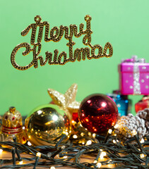letrero dorado de feliz navidad en ingles en fondo verde y decorado con objetos navideños....