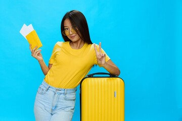 Asian woman traveling with yellow suitcase and tickets with passport in hand, tourist traveling by plane and train with luggage on blue background