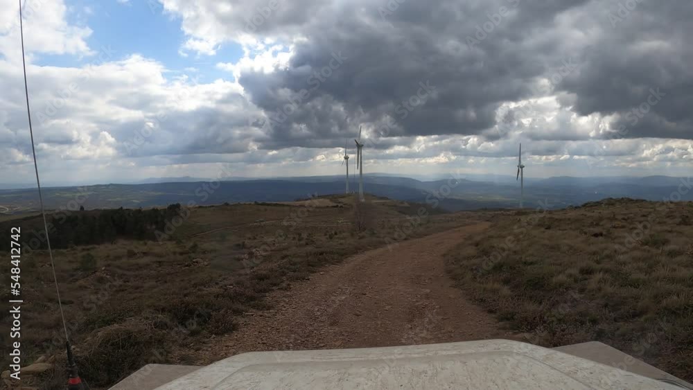 Wall mural Video shot from a Land Rover Defender on an overland trip on a dirt road up the mountain through a forest, a field or a group of electricity generating windmills. Wind turbines, a gray, dark, rainy da