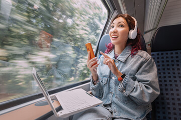 A girl with a laptop and a smartphone rides on a modern train and uses public Wi-Fi Internet