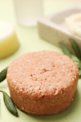 Solid shampoo bar and leaf on green background, closeup. Hair care