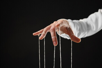 Woman pulling strings of puppet on black background, closeup