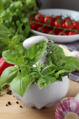 Mortar with fresh herbs, garlic and black peppercorns on wooden table, closeup
