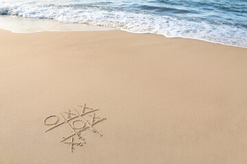 Tic tac toe game drawn on sand near sea, space for text