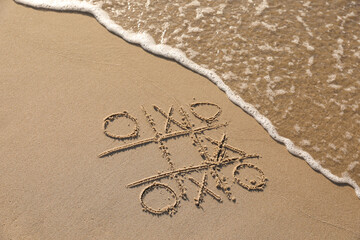 Tic tac toe game drawn on sand near sea, space for text
