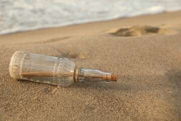Fototapeta na wymiar SOS message in glass bottle on sand near sea, space for text