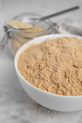 Sesame flour in ceramic bowl on white marble table, closeup