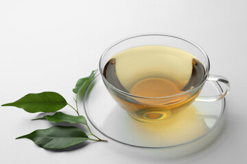 Fresh green tea in glass cup with saucer and leaves on white table