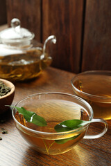 Fresh green tea in glass cups and leaves on wooden table