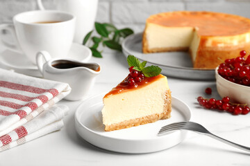Piece of delicious caramel cheesecake with red currants and mint served on white marble table