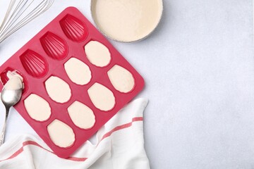 Baking mold for madeleine cookies with batter and spoon on white table, flat lay. Space for text